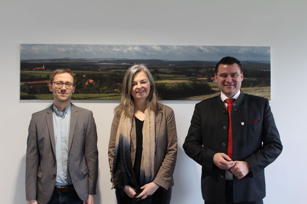 drei Personen stehen vor einem Hintergrundbild und lächeln