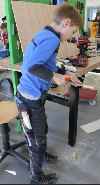 Ein junge steht an einer Werkbank und sägt an einem Stück Holz