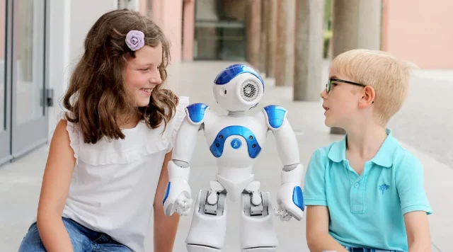 Zwei Kinder sitzen neben einem Roboter auf dem Boden.