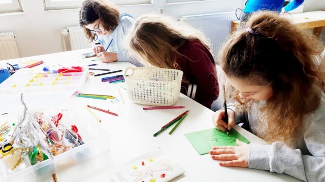 Kinder basteln mit Stiften und Papier am Tisch.