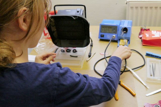 eine Jugendliche arbeitet mit Elektronik und Messgeräten an einem Tisch.