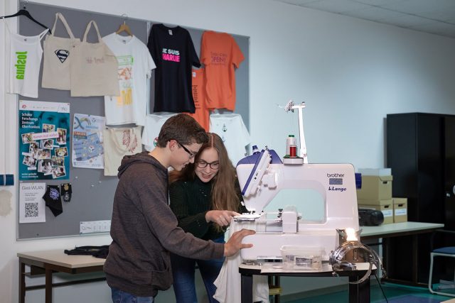 zwei junge Menschen schneidern zusammen ein Kleidungsstück an einer Nähmaschine