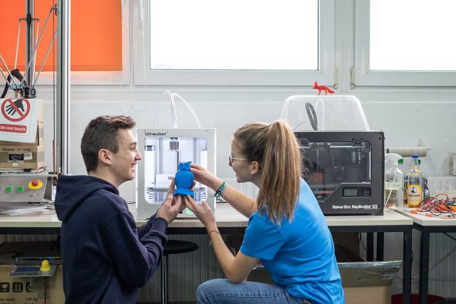 zwei junge Erwachsene betrachten ein blaues Model einer Eule aus dem 3D-Drucker
