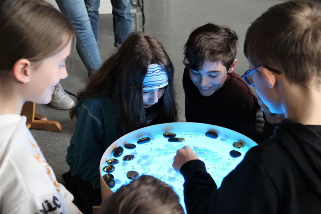 Kinder schauen in Wasserbecken, in dem einige Steine schwimmen und andere unter Wasser sind