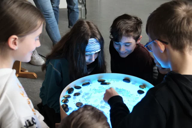 Kinder schauen in Wasserbecken, in dem einige Steine schwimmen und andere unter Wasser sind
