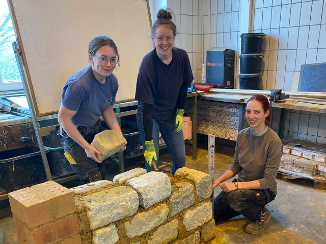 drei junge Frauen mauern eine kleine Steinmauer aus Naturstein in einem Innenraum