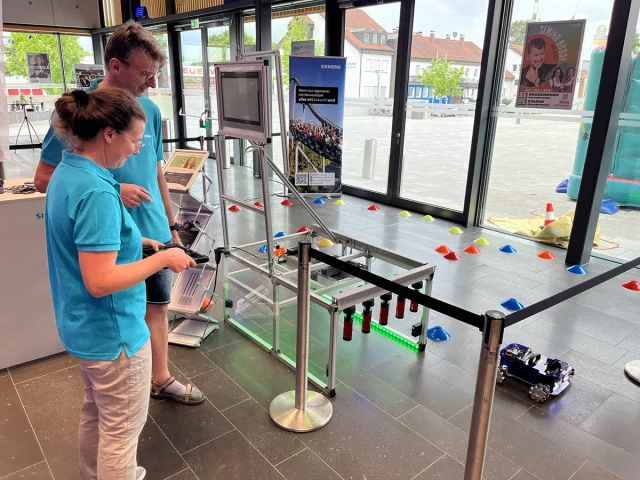 Zwei Personen bei einem Roboterwettbewerb neben einem Parcours.