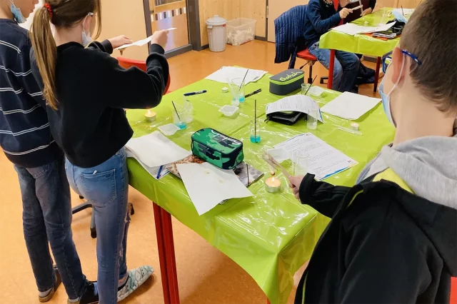 Kinder beim Experimentieren im Klassenraum an grünen Tischen.