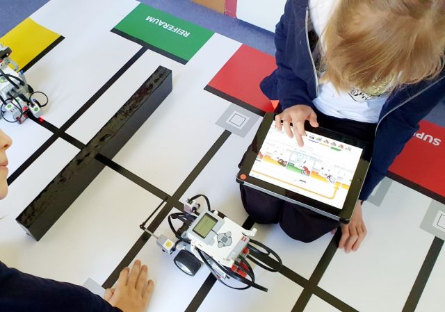 Zwei Schuler steuern einen Roboter mit einem Tablet