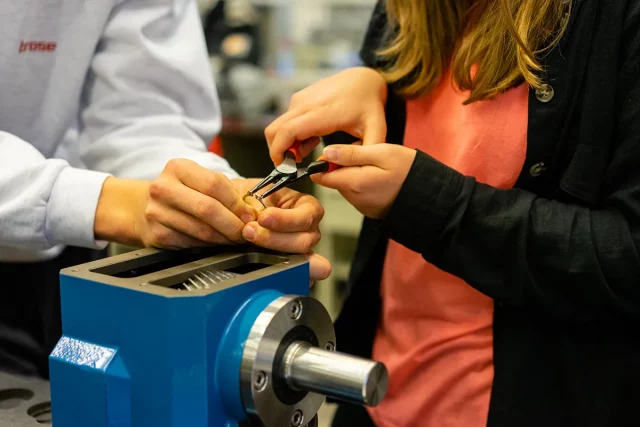 zwei Menschen biegen kleinen Metallring mit einer Zange