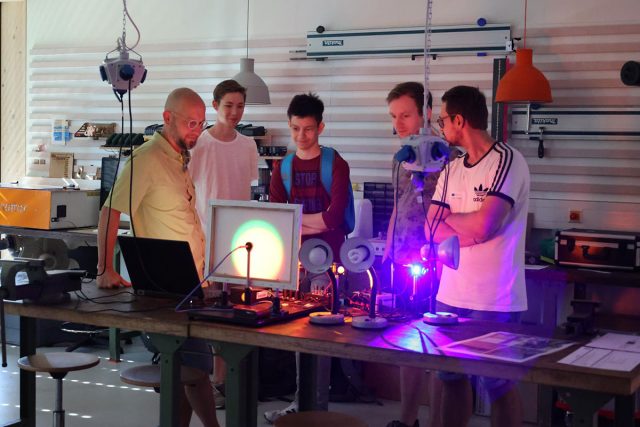 eine Gruppe junger Männer stehen an einem Tisch mit Lichtexperimenten