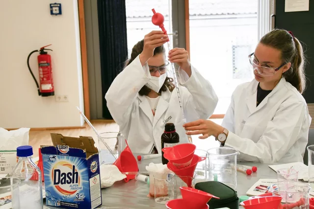 zwei junge Frauen in Laborkitteln experimentieren mit chemischen Flüssigkeiten