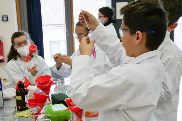 Kinder in Laborkitteln experimentieren mit Pipetten und Reagenzgläsern