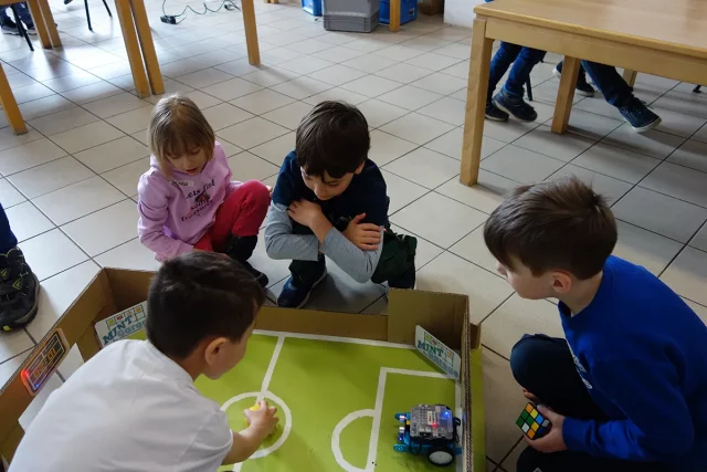 Kinder spielen mit einem Mini Roboter Fussball.