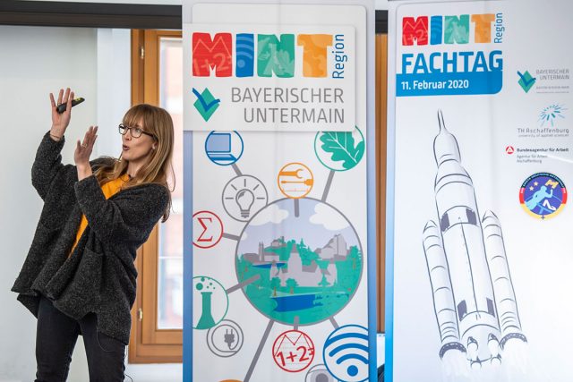 Frau steht neben Roll-ups der MINT-Region bayrischer Untermain