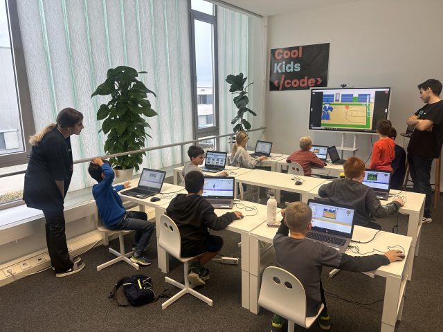 Gruppe von Kindern in einem Kursraum mit Laptops beim Programmieren.