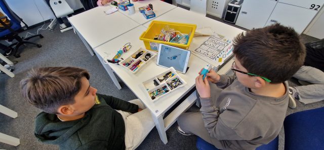 Kinder arbeiten an einem Robotikprojekt mit einem Tablet und Bausätzen.