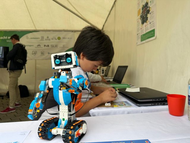 Kind sitzt an einem Tisch mit einem Roboter im Vordergrund.