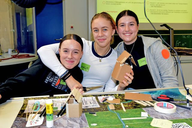 drei Mädchen zeigen ihre selbst gebauten Miniaturhäuser aus Pappe