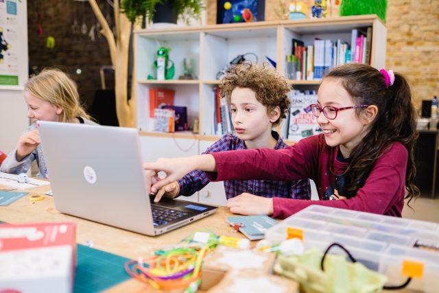 Kinder arbeiten gemeinsam an einem Laptop in der Bibliothek.