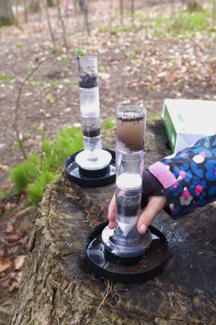Kind untersucht Wald Bodenschichten mit einem Experiment.