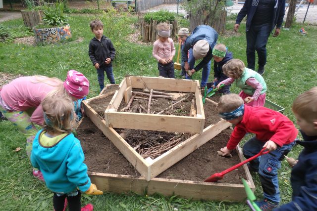 Gruppe von Kindern baut ein Hochbeet mit Holzrahmen.