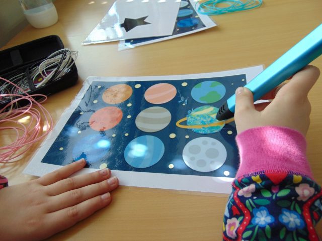 Kind malt Planeten mit 3D-Stift auf Arbeitsblatt.