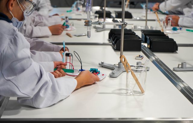Schülerhände in weißen Kitteln an einem Labortisch.