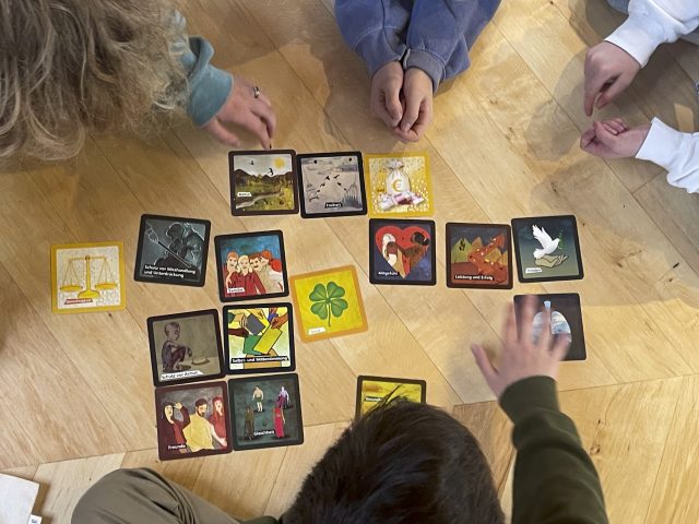 Mehrere Hände spielen mit bunten Karten auf dem Boden.