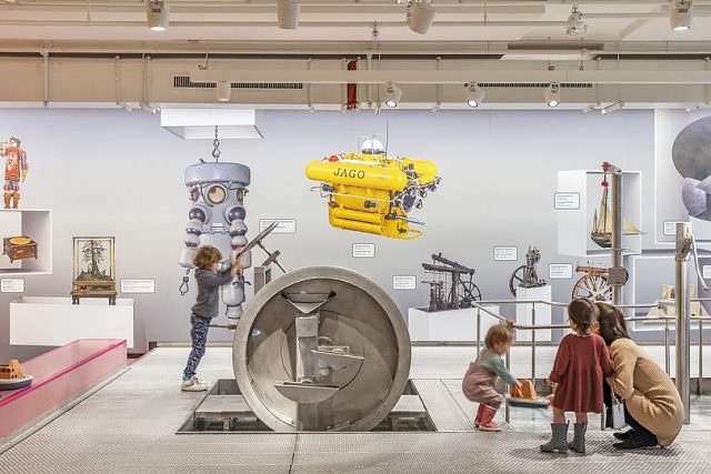 Kinder spielen in einer Museumsausstellung mit Maschinenmodellen.