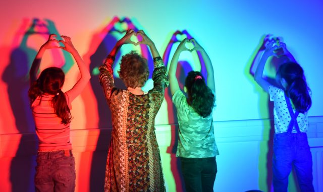 Menschen kreieren Herzschatten mit buntem Licht an der Wand.