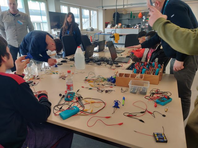 Mehrere Personen arbeiten an elektronischen Projekten an einem Tisch.