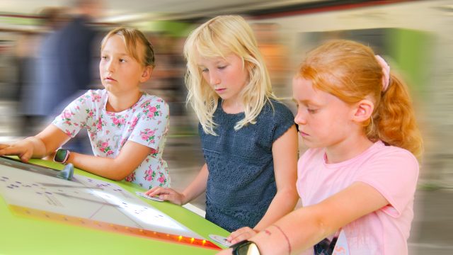 Drei Kinder am Tisch mit buntem Hintergrund