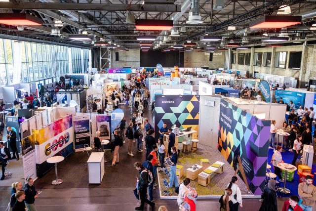 Menschen stöbern auf einer bunten Messe mit vielen Ständen.