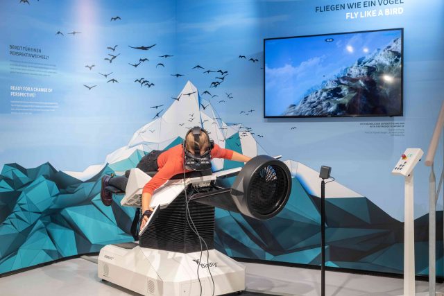 Person in VR-Simulator fliegt über einen Berg.