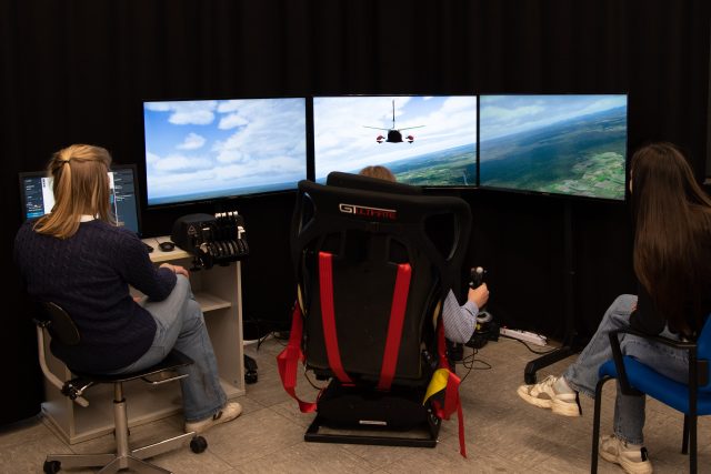 Personen bedienen Flugsimulator mit mehreren Bildschirmen.