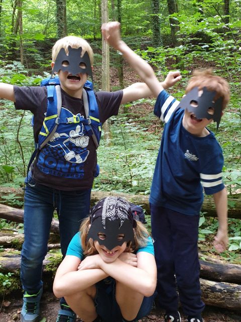 Drei Kinder tragen Batman-Masken im Wald.