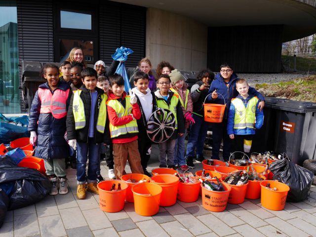 Kinder sammeln Müll mit orangenen Eimern.
