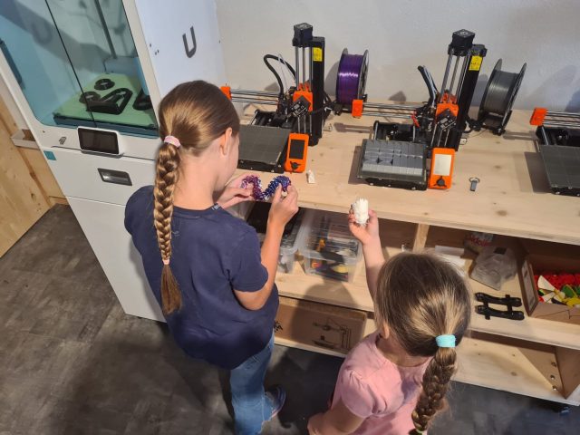 Zwei Mädchen bedienen 3D Drucker auf einem Tisch.