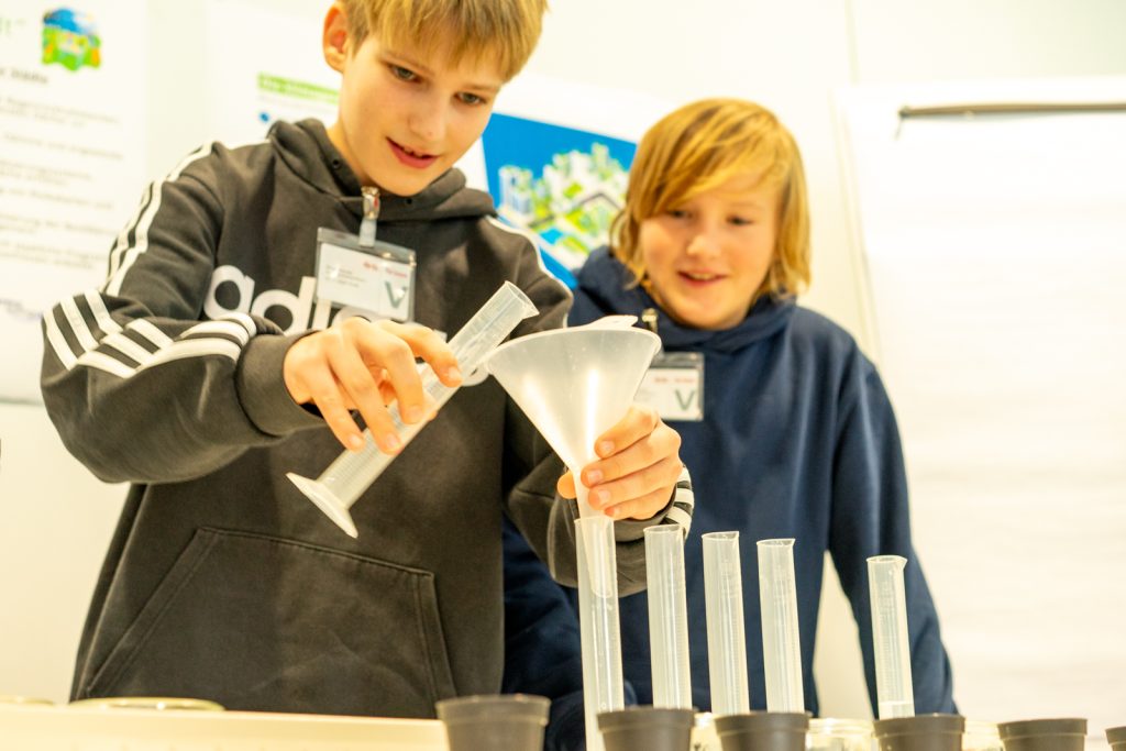 Kinder experimentieren mit Trichtern und Messzylindern.