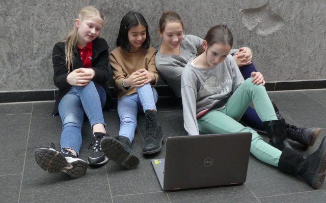 Vier Jugendliche sitzen nebeneinander und schauen auf einen Laptop.