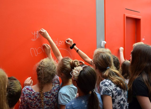 Kinder malen mit Kreide an eine rote Wand.