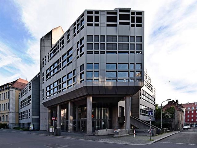 Modernes Gebäude aus Beton mit großen Fenstern und Straßenszene.