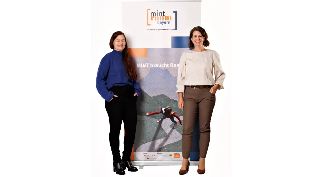 Petra Scheuermayer und Susanne Knotzer stehen links bzw. rechts neben dem Rollup vom MINTraum bayern.