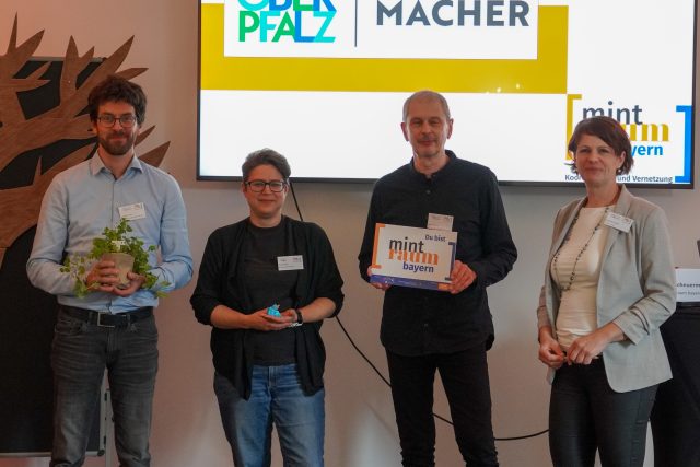 Vertreter und Vertreterinnen der MINT-Region MINTerMACHER mit Susanne Knotzer. Im Hintergrund ist auf einem Bildschirm das Logo der MINT-Region zu sehen.